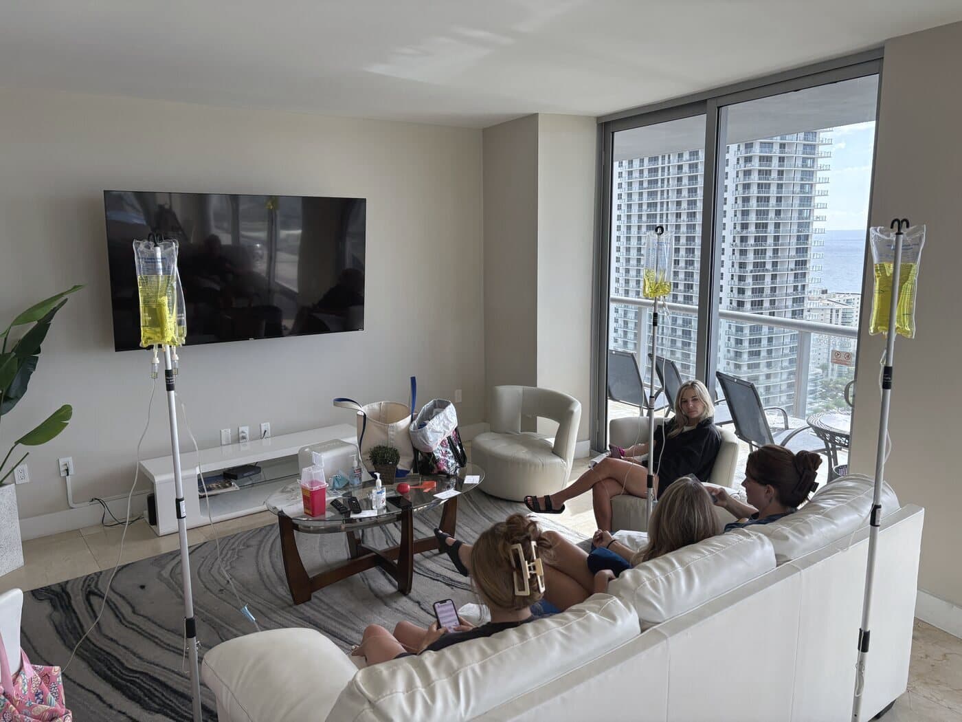 A group of friends relaxing with Iso IV hydration drips in a South Florida high-rise overlooking the skyline